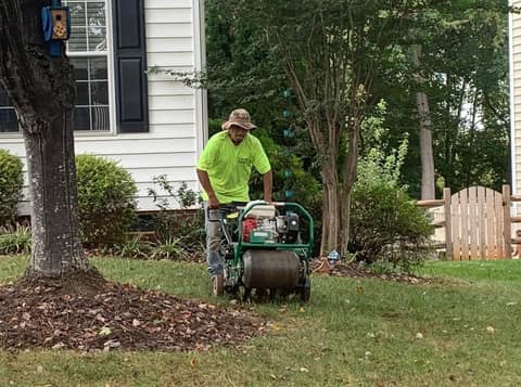 Crew member running a core aerator across a front lawn