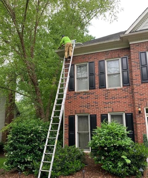 Crew member clearing gutters from a ladder