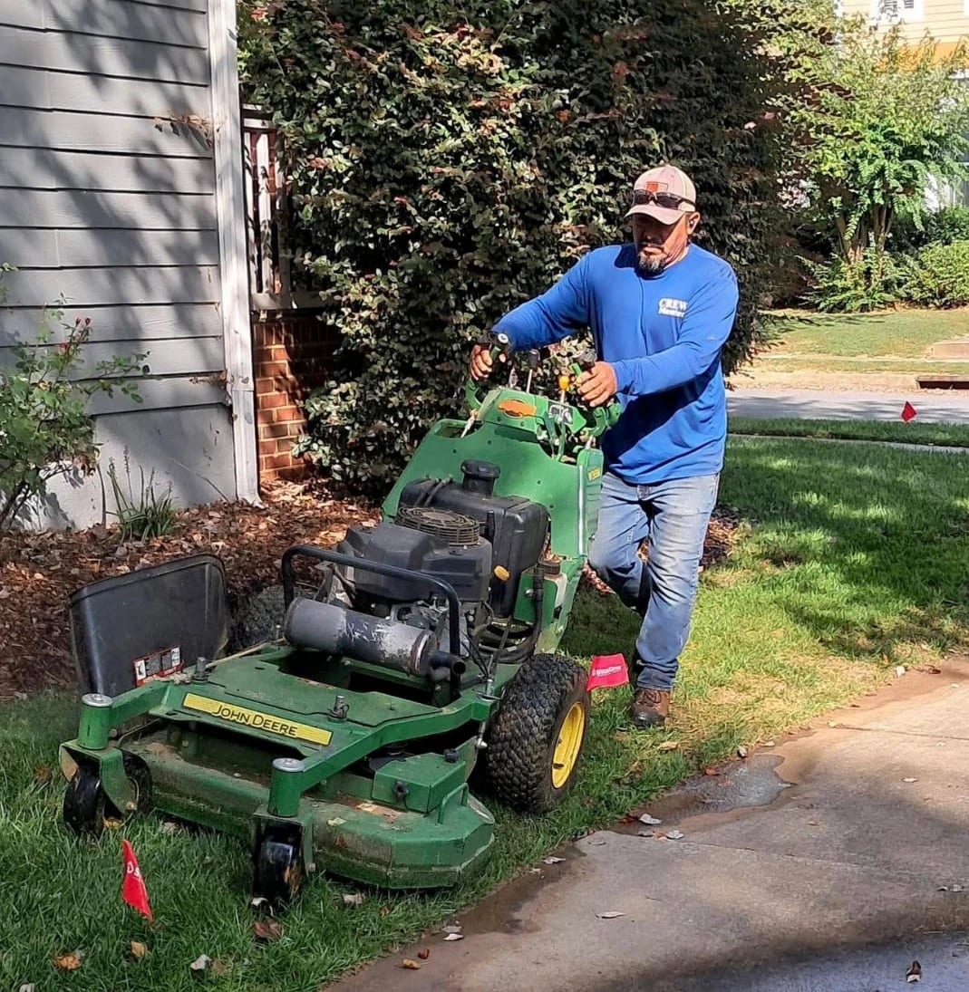 Crew member mowing a front lawn with a walk-behind mower