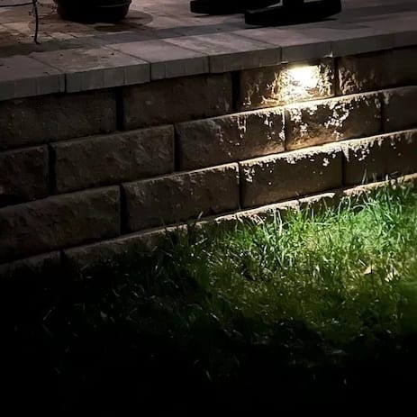 Low-voltage light glowing under the cap of a stone seat wall at night