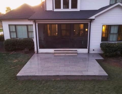 Finished classic paver patio behind a screened porch at dusk