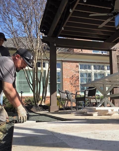 Crew member setting travertine pavers under a pergola