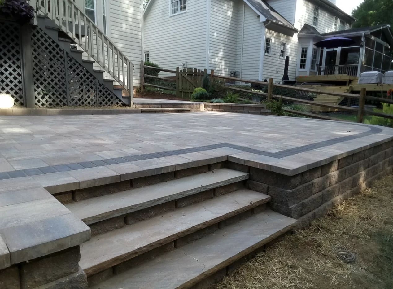 Raised paver patio with a charcoal border, block wall and stone steps